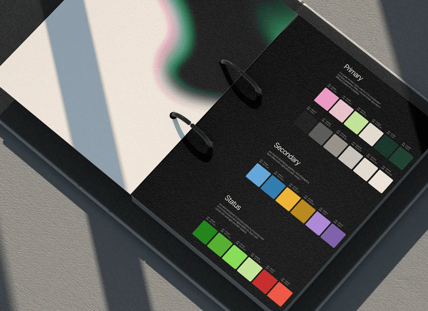 Livre d'échantillons de couleurs présentant des palettes primaires, secondaires et de statut sur un fond noir, avec des ombres diagonales visibles.