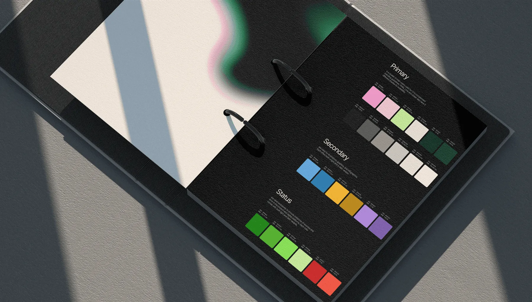 Cahier ouvert avec un nuancier de couleurs sur page noire divisée en sections : primaire, secondaire et statut, avec des carrés de différentes couleurs.