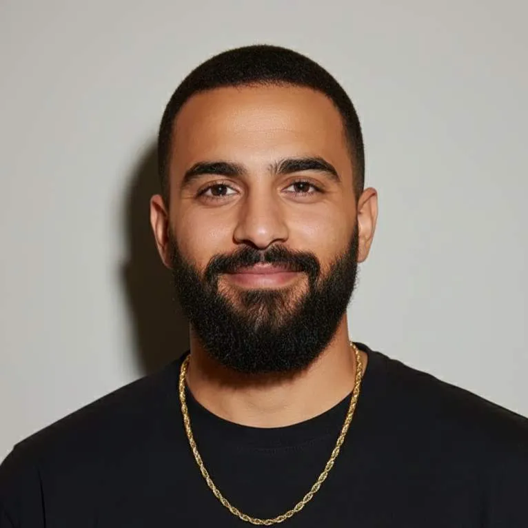 Portrait d'un homme souriant avec une barbe, portant un t-shirt noir et une chaîne en or.