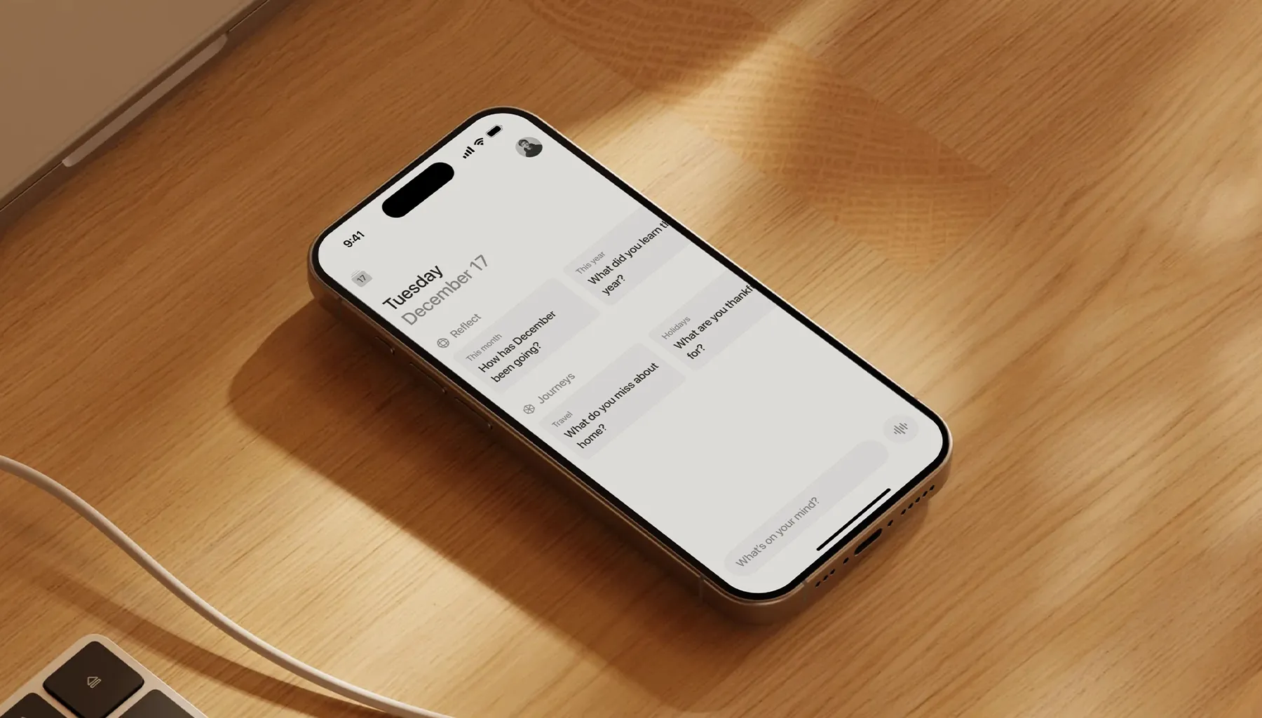 Un smartphone posé sur une surface en bois avec une application affichant la date du mardi 17 décembre et des questions de réflexion.